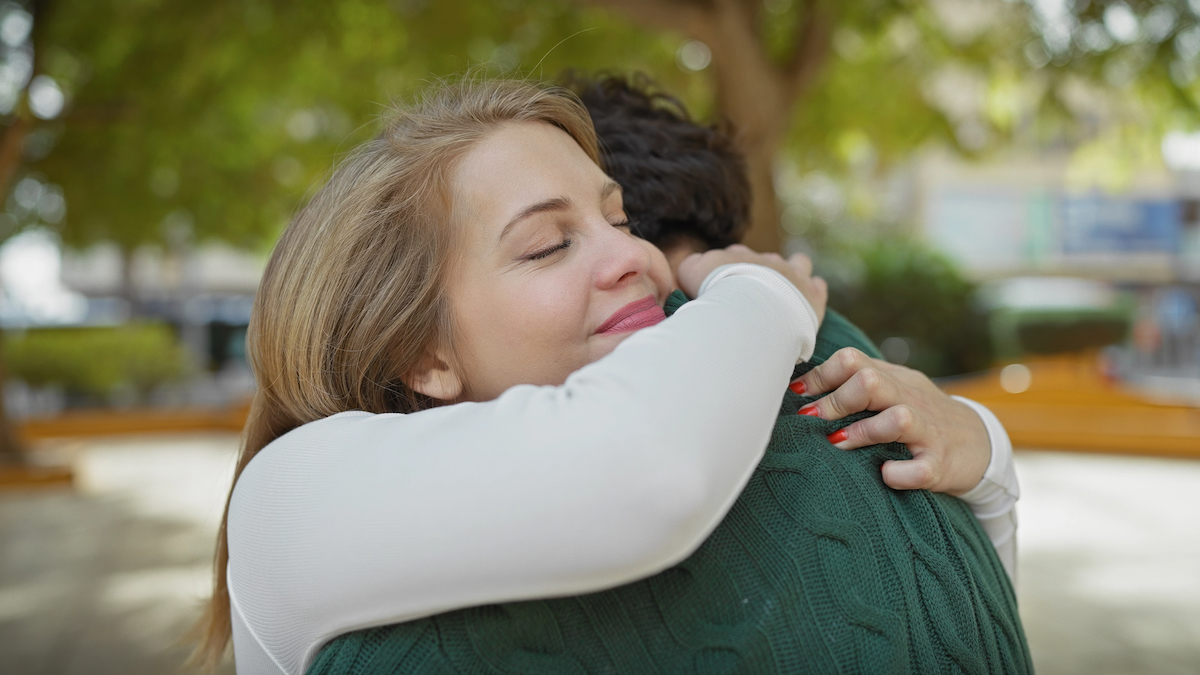 A woman embraces a man in a serene park, expressing affection and joy in a sunny outdoor setting.